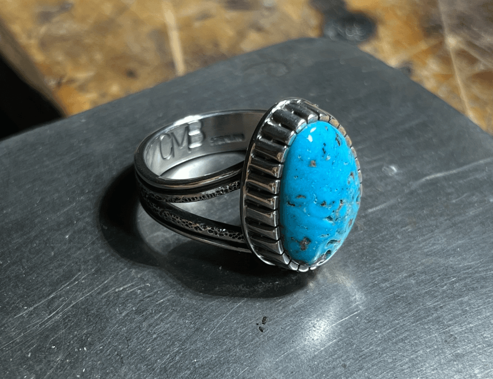 Handmade silver ring with turquoise stone in fluted bezel resting on a silversmith anvil