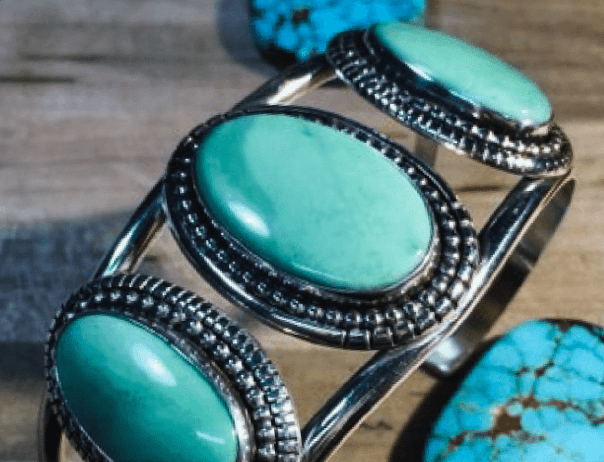 Silver cuff bracelet with three green turquoise ovals in beaded bezels beside loose turquoise stones