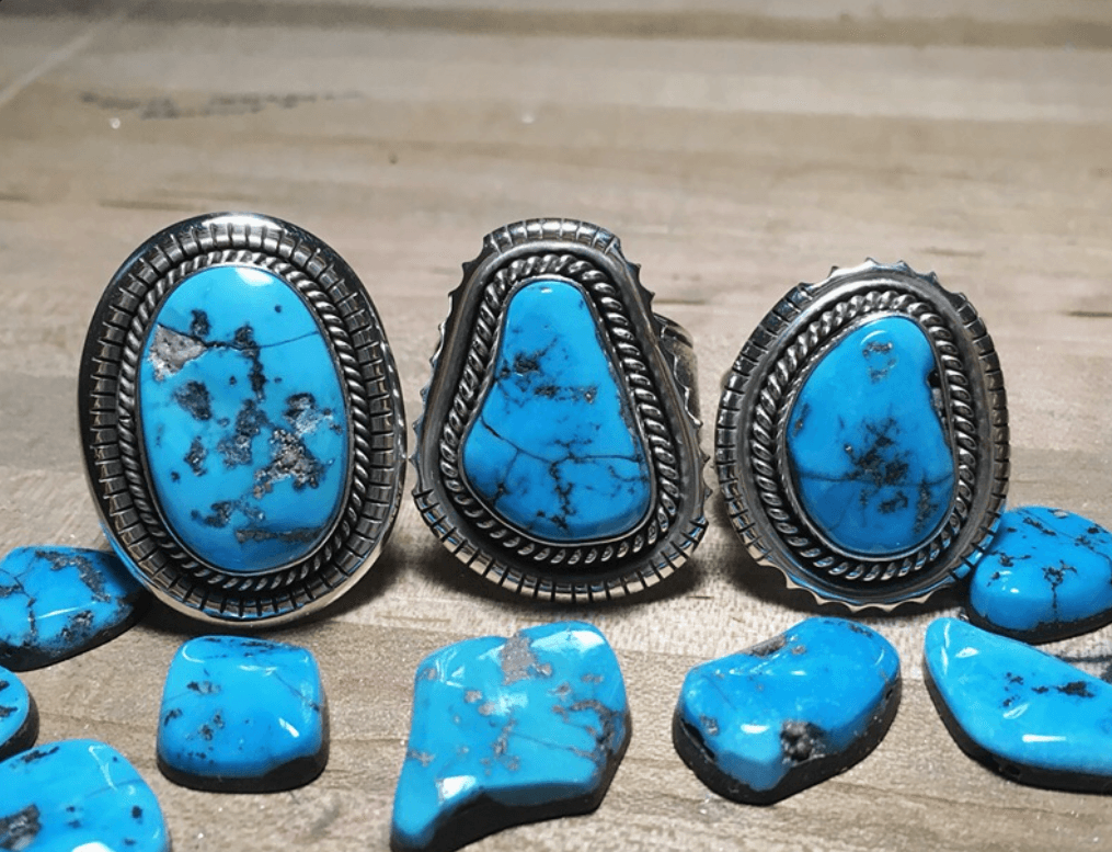 Three handmade silver rings with Kingman turquoise stones and loose cabochons on a workbench