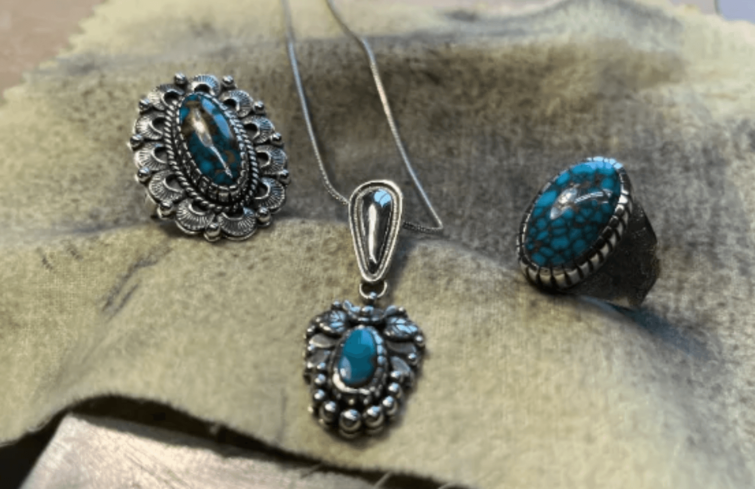 Finished handmade silver pieces — a stamped ring, a beaded pendant, and a spiderweb turquoise ring — laid out on hide