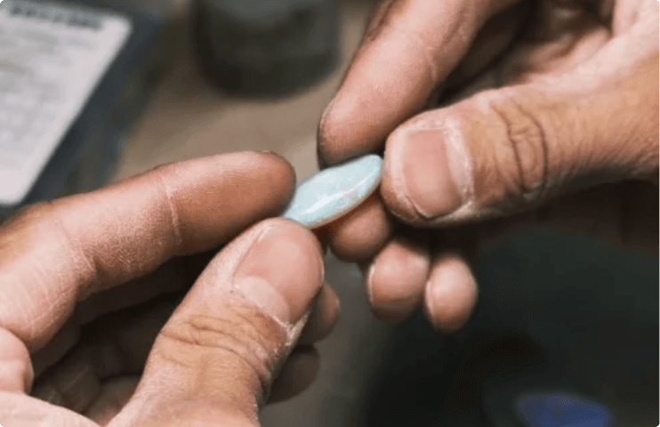 The silversmith's hands holding a hand-cut opal cabochon up to the light at the bench